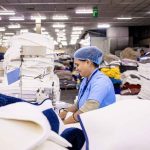 A woman operates machinery in a factory surrounded by stacks of white towels, focusing on her task efficiently.